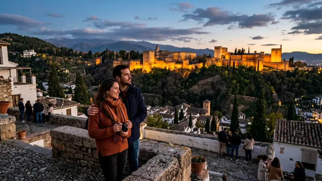 Couple standing at Mirador de San Nicolás in the Albaicín at sunset, the Alhambra lit in warm amber light across the Darro valley